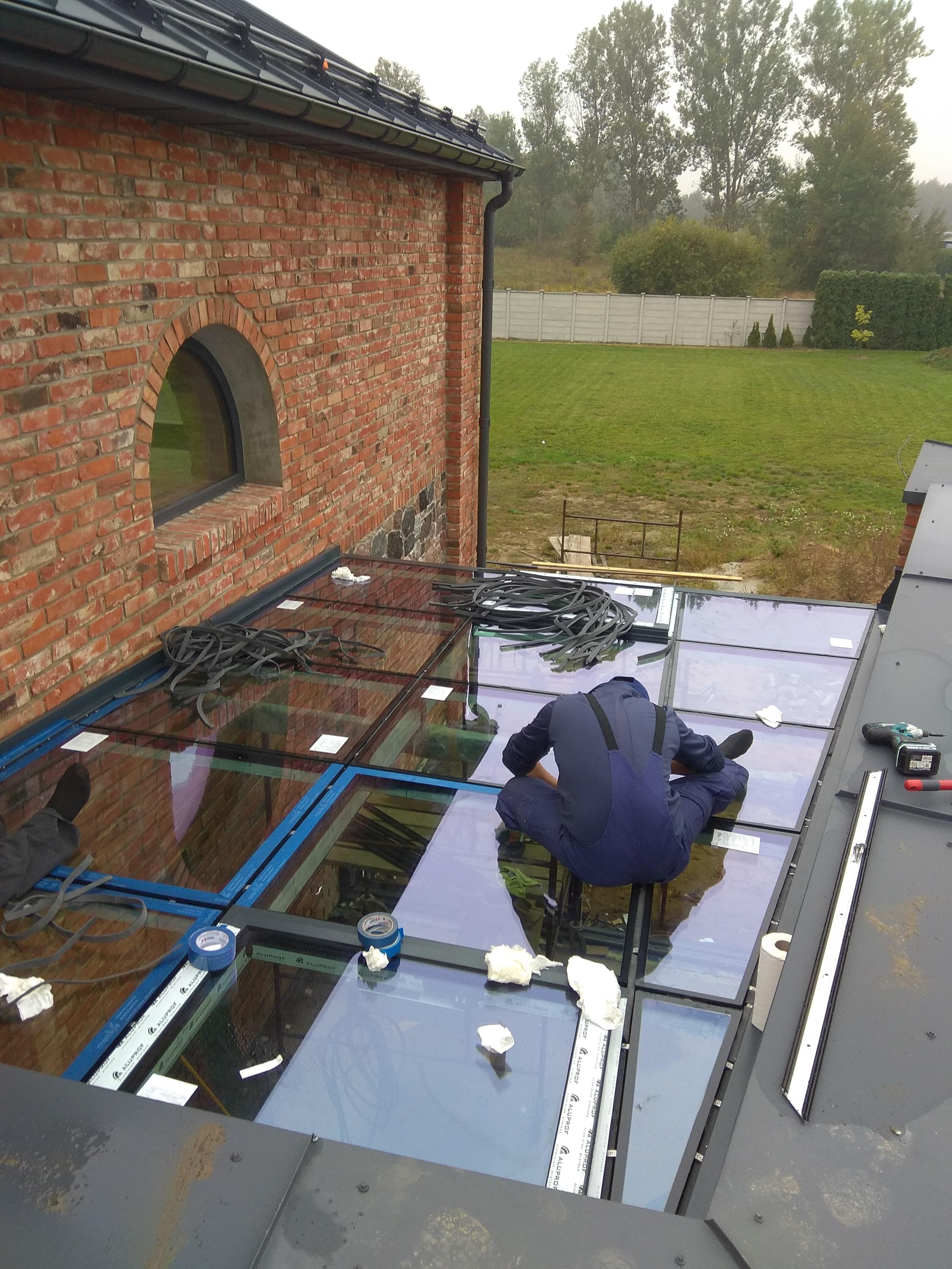 Aluminiowa fasada dwukondygnacyjna, drzwi przesuwne, drzwi wejściowe i aluminiowy przedsionek ze szklanym dachem.