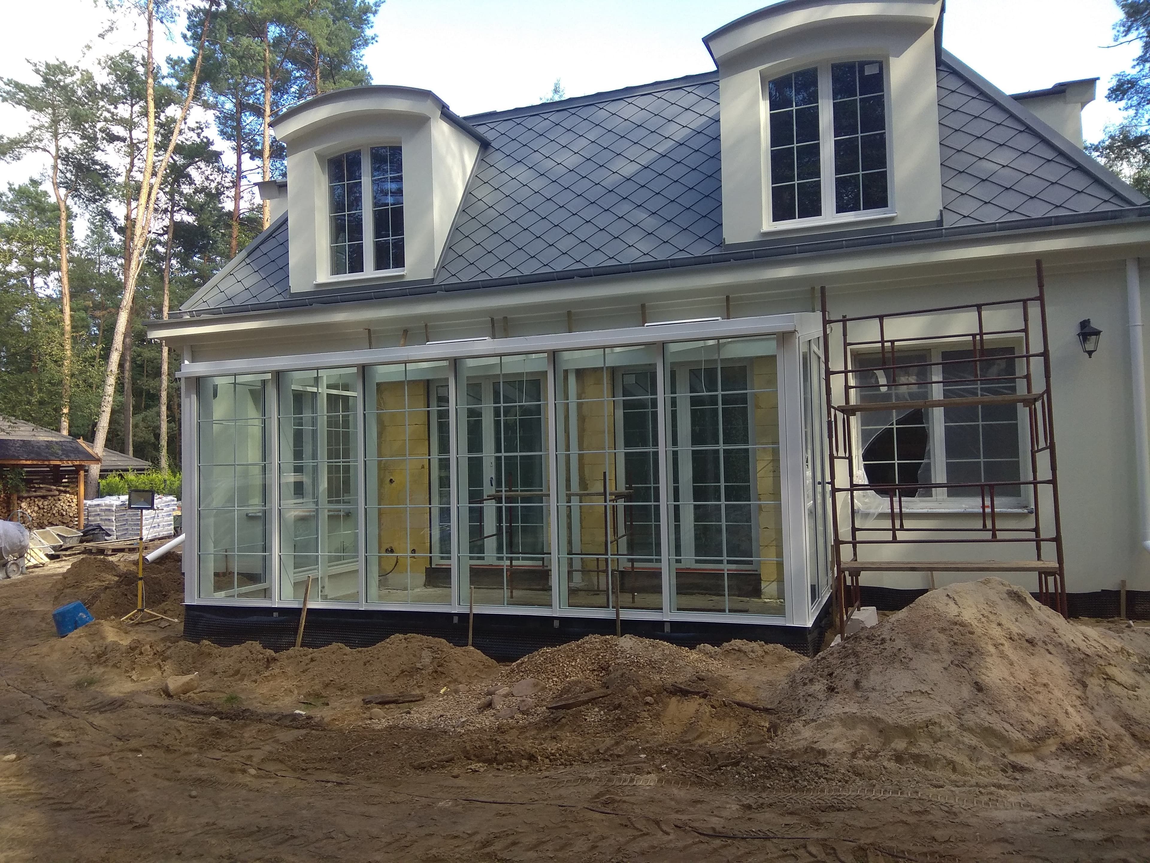 Ogród zimowy ze szklanym dachem na konstrukcji aluminiowej, białe okna aluminiowe z łukami i szprosami.