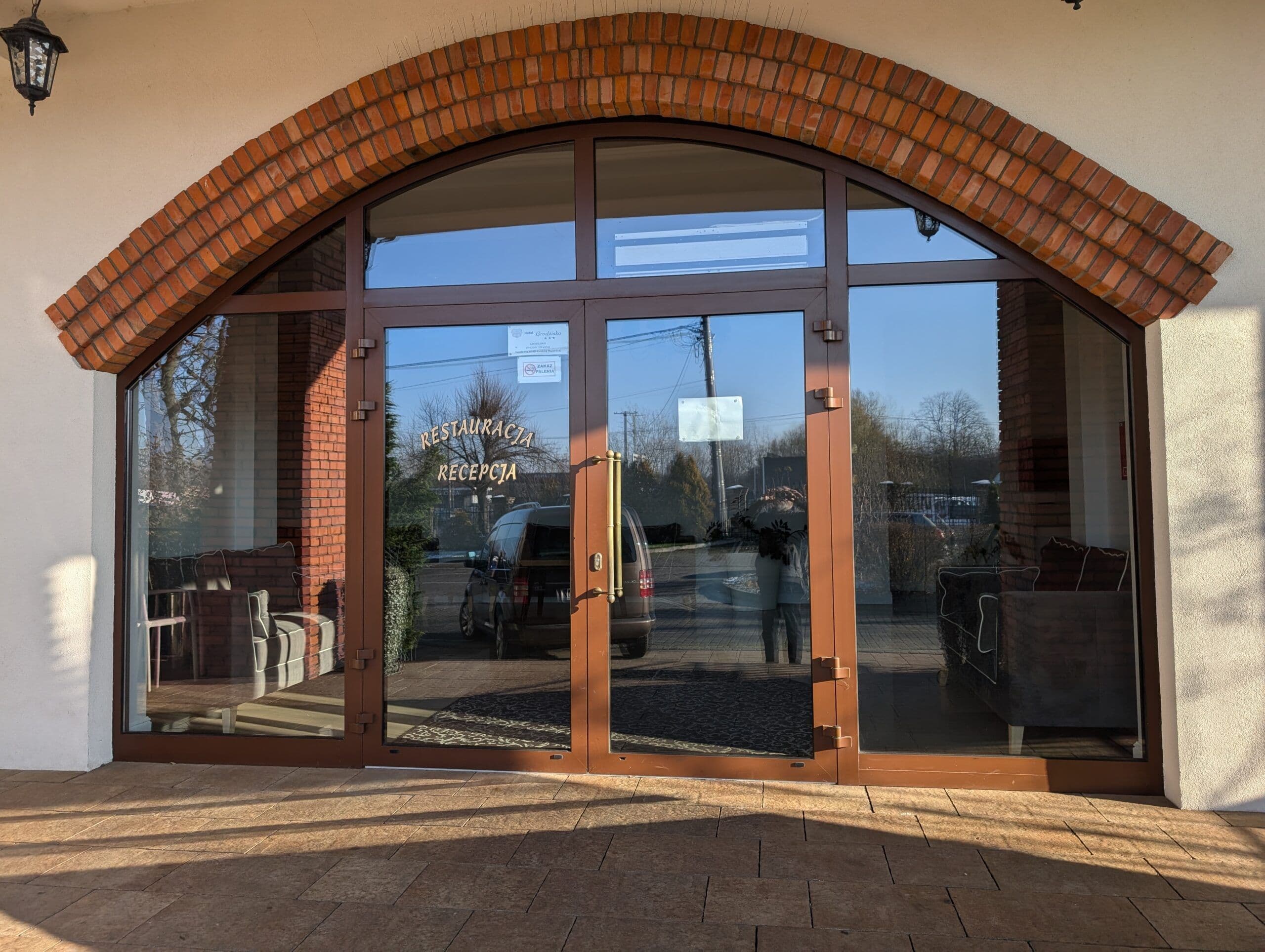 Okna aluminiowe w kolorze drewna oraz aluminiowe drzwi wejściowe z łukowymi doświetlami.