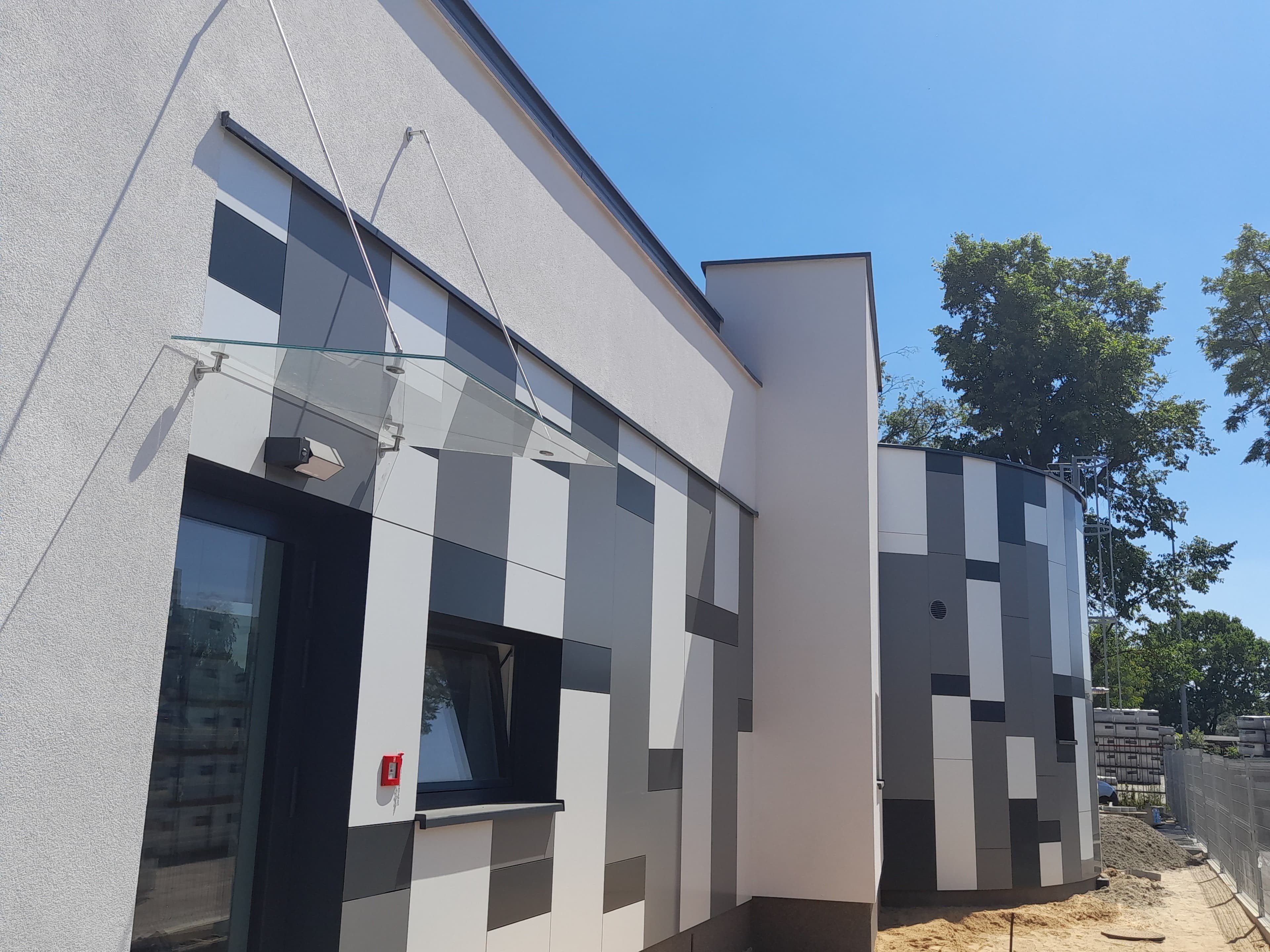 Fasada szklana oraz elewacja wielokolorowa na konstrukcji aluminiowej w budynku na planie koła, plus daszek szklany.