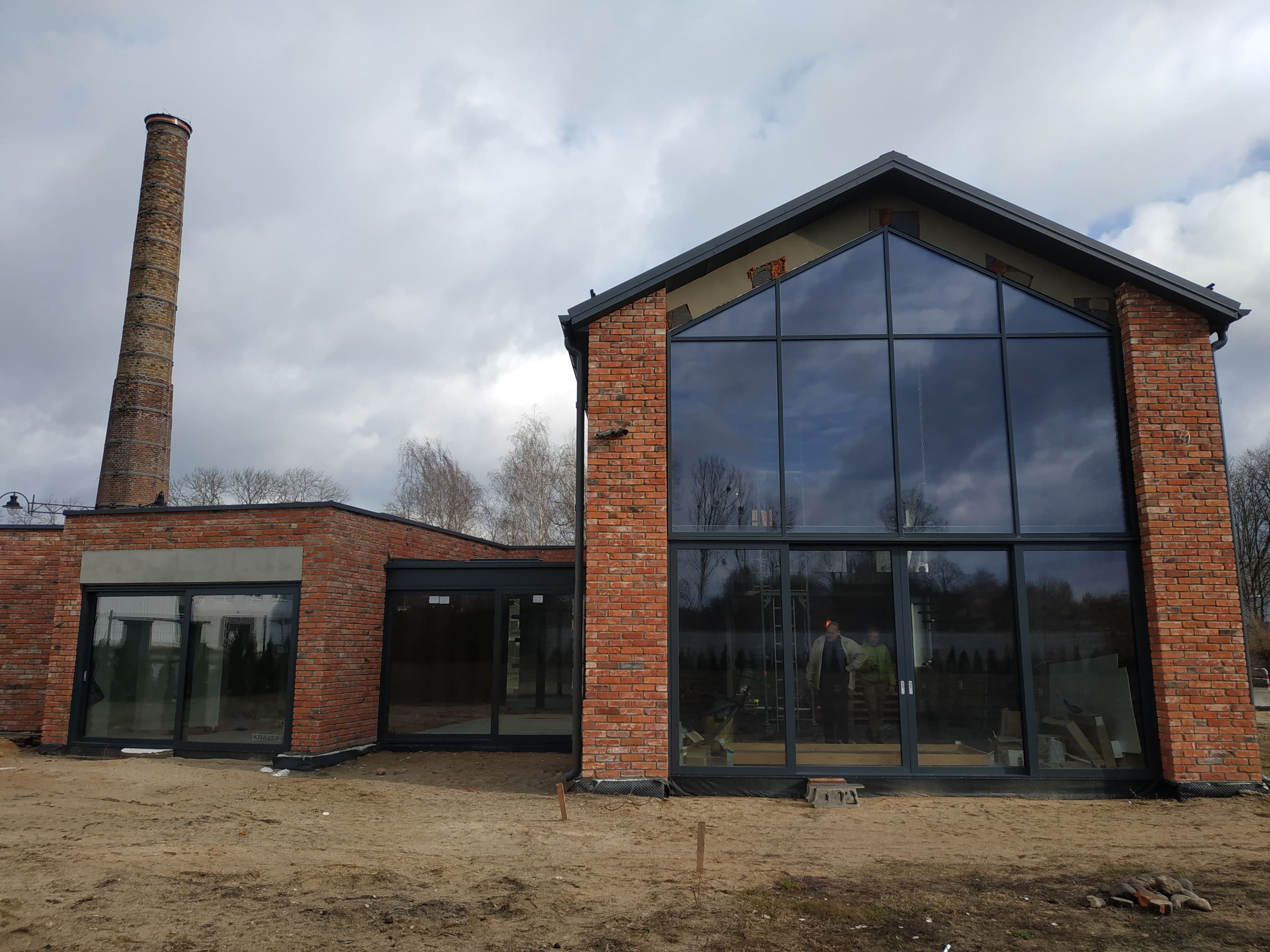 Aluminiowa fasada dwukondygnacyjna, drzwi przesuwne, drzwi wejściowe i aluminiowy przedsionek ze szklanym dachem.